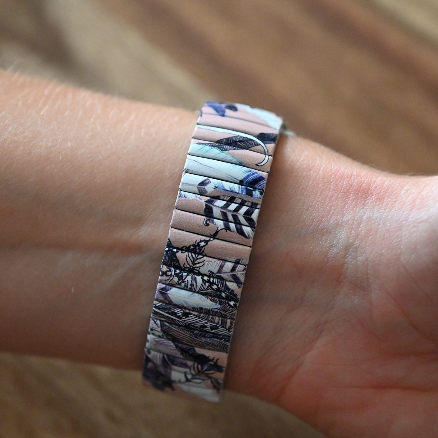 Armband mit Federdesign in Lachsfarbe und Blau, getragen am Handgelenk. Detailliertes Muster auf schmalem Band.