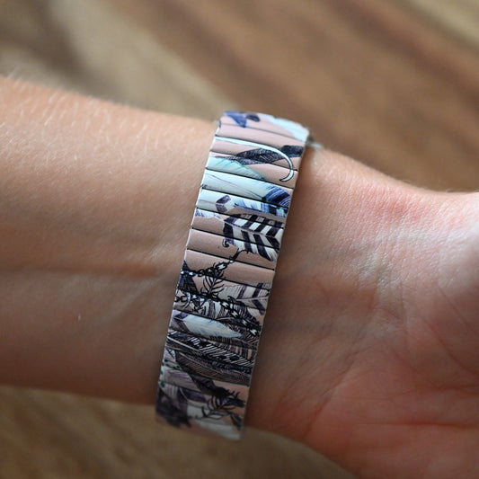 Armband mit Federdesign in Lachsfarbe und Blau, getragen am Handgelenk. Detailliertes Muster auf schmalem Band.