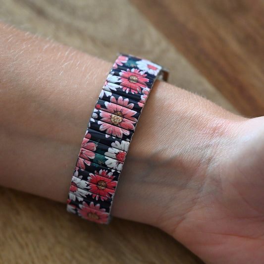 Elastisches Armband mit floralem Muster aus rosa und weißen Margeriten auf schwarzem Hintergrund am Handgelenk