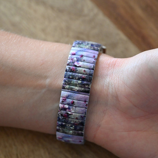 Buntes Armband mit Blumenmuster in Lila- und Blautönen auf einem Handgelenk, Nahaufnahme auf Holzuntergrund