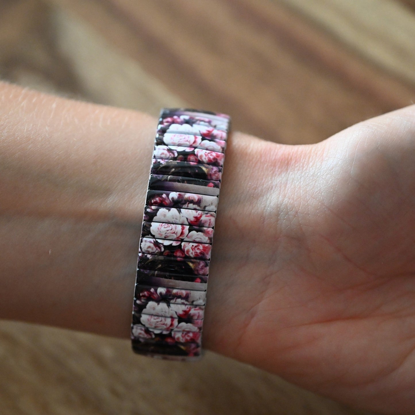 Armband mit Blumenmuster, rosa Pfingstrosen auf dunklem Hintergrund, am Handgelenk getragen, Nahaufnahme