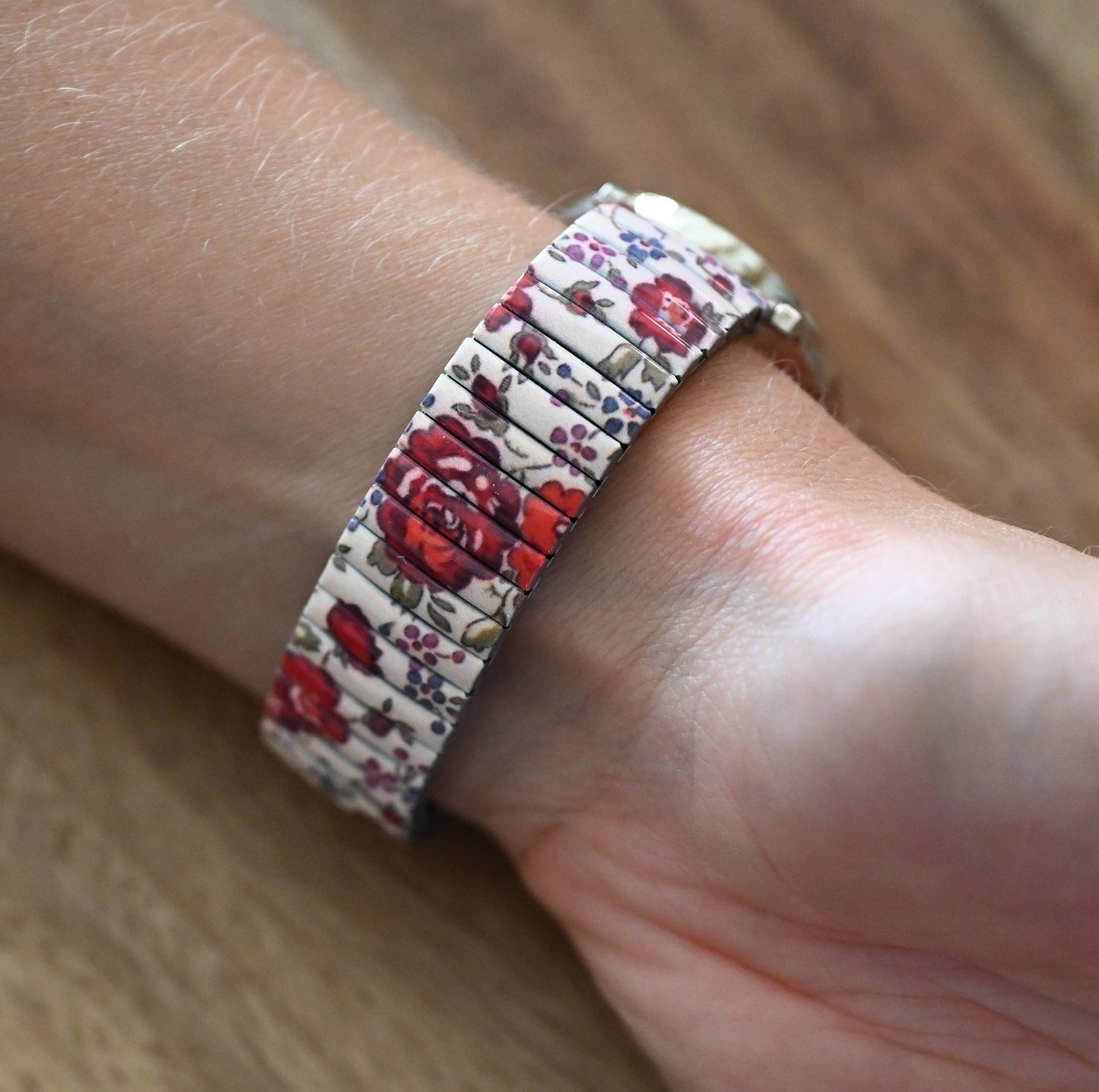 Armband mit rotem Blumenmuster auf weißem Grund, getragen am Handgelenk auf Holzuntergrund
