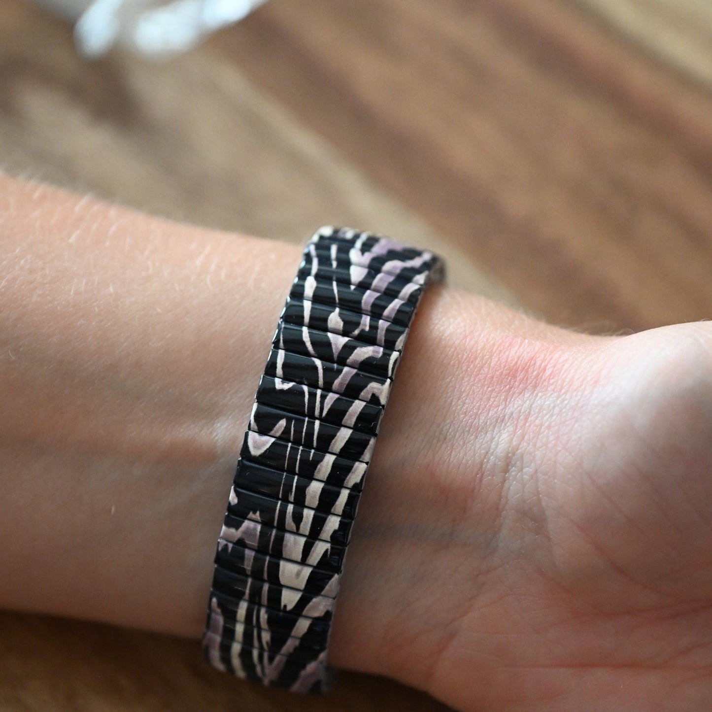 Elastisches Armband mit schwarz-beigem Zebramuster auf Handgelenk, modisches Accessoire auf Holzuntergrund