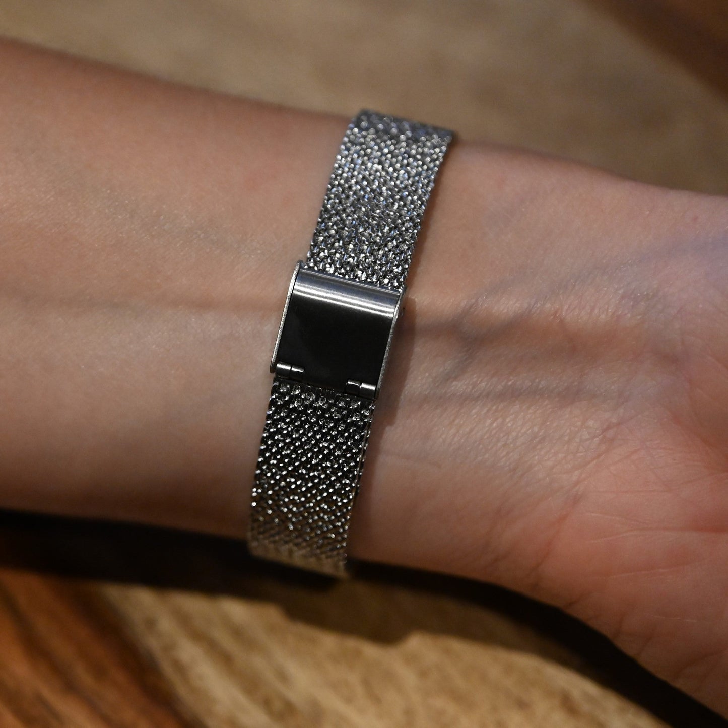 Silberne Armbanduhr mit funkelndem Metallarmband am Handgelenk, auf Holzuntergrund fotografiert