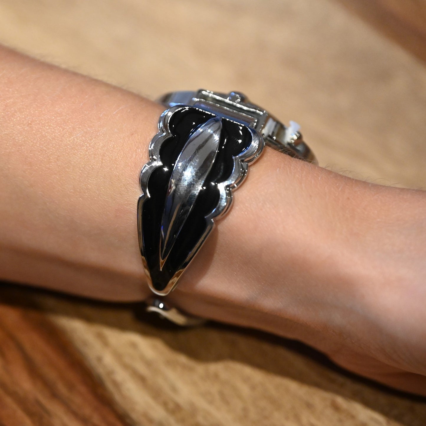 Elegante schwarze und silberne Armbanduhr mit blattförmigem Design am Handgelenk, auf Holzuntergrund