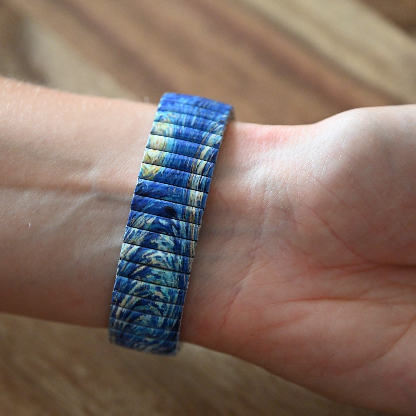 Blaues Armband mit marmoriertem Muster auf Handgelenk, elastisches Design mit schmalen Segmenten, Holzhintergrund