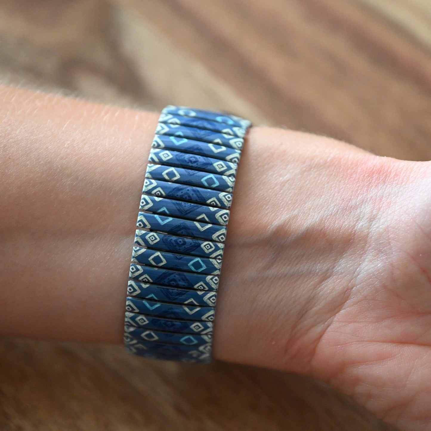 Elastisches Armband in Blautönen mit geometrischem Muster, am Handgelenk getragen, auf Holzuntergrund