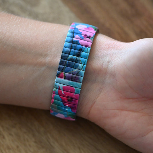 Buntes Armband mit Blumenmuster in Fuchsia und Türkis auf Metall-Stretchband am Handgelenk getragen
