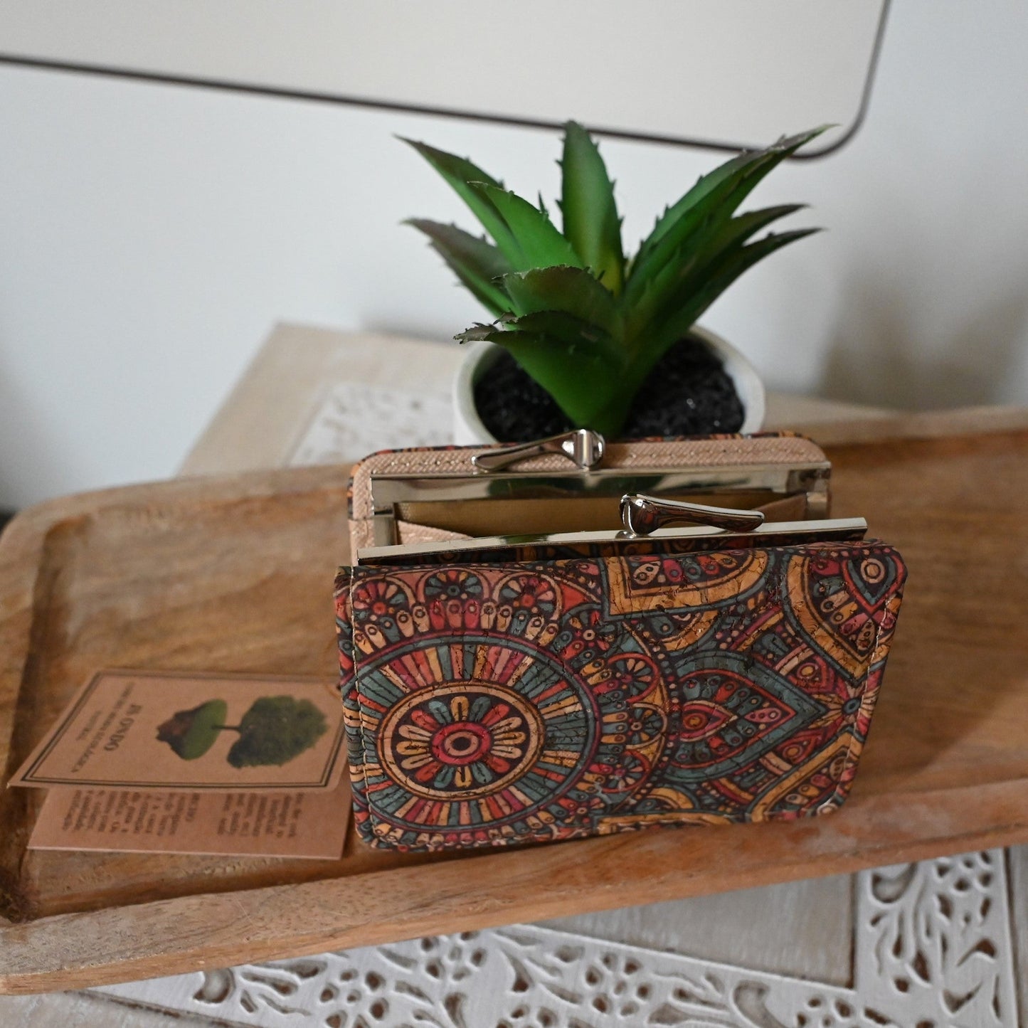 Bunte Kork-Geldbörse mit Mandala-Muster neben Sukkulente und Buch auf Holztisch, Boho-Stil Accessoire