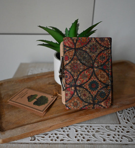 Kompakter Kork-Geldbeutel mit buntem Mandala-Muster neben Pflanze und Holzschnitzerei auf rustikalem Tisch