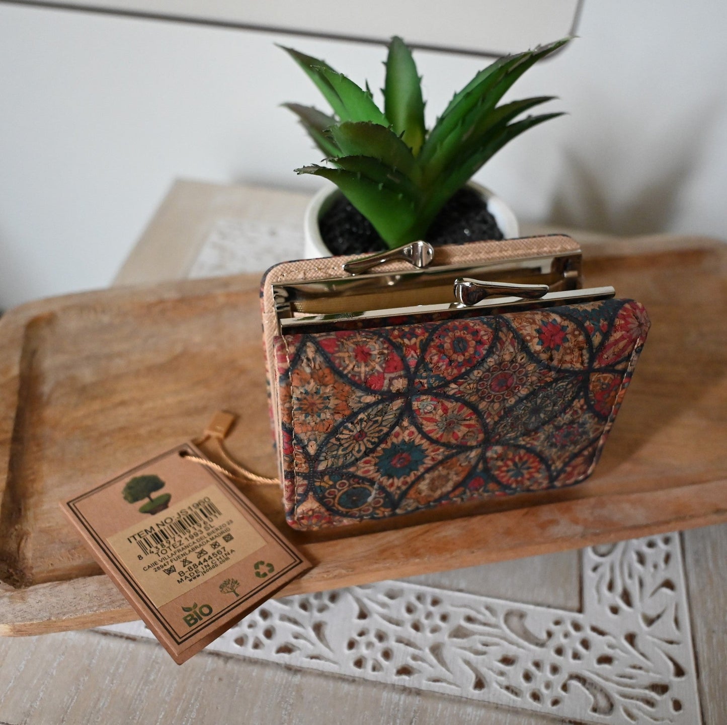Kleiner Geldbeutel aus Kork mit Blumenmuster neben Pflanze und Bio-Etikett auf Holzoberfläche mit Spitzendeckchen