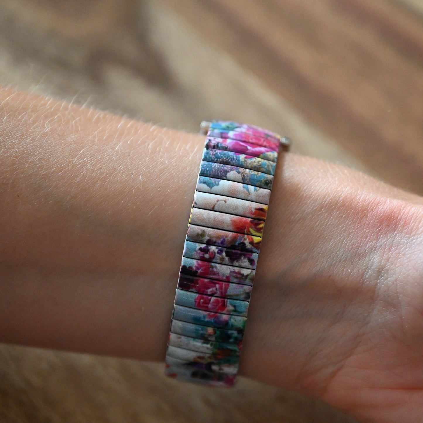 Buntes Armband mit Blumenmuster auf Handgelenk, elastisches Metallband mit farbenfrohem Blumendesign