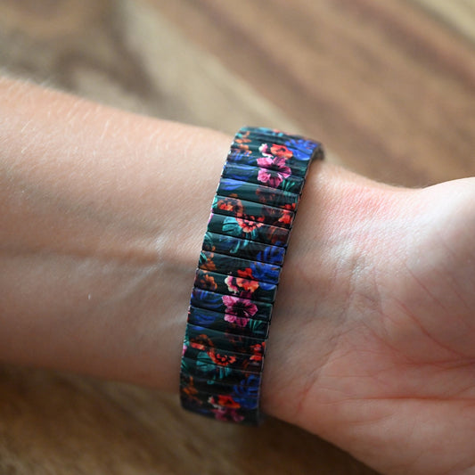 Elastisches Armband mit buntem tropischen Blumenmuster auf dunklem Grund, am Handgelenk getragen