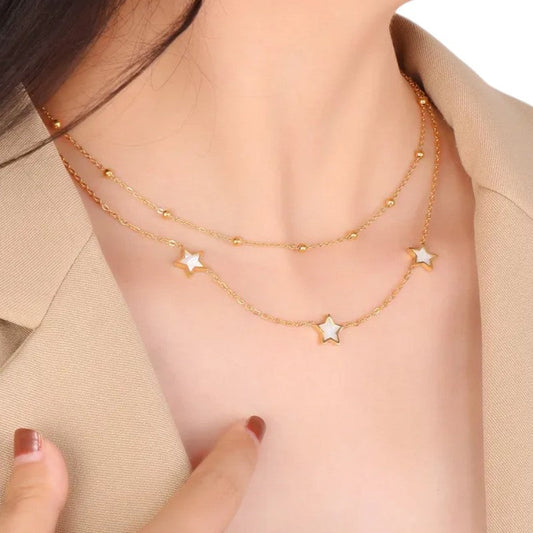 Doppelte goldene Halskette mit Perlmutt-Sternen und kleinen Perlen auf Dekolleté einer Frau in beigem Oberteil