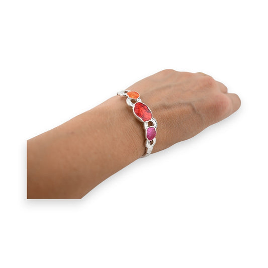 Elastisches Armband mit bunten Steinen in Orange, Rot und Pink auf silbernem Band, am Handgelenk getragen