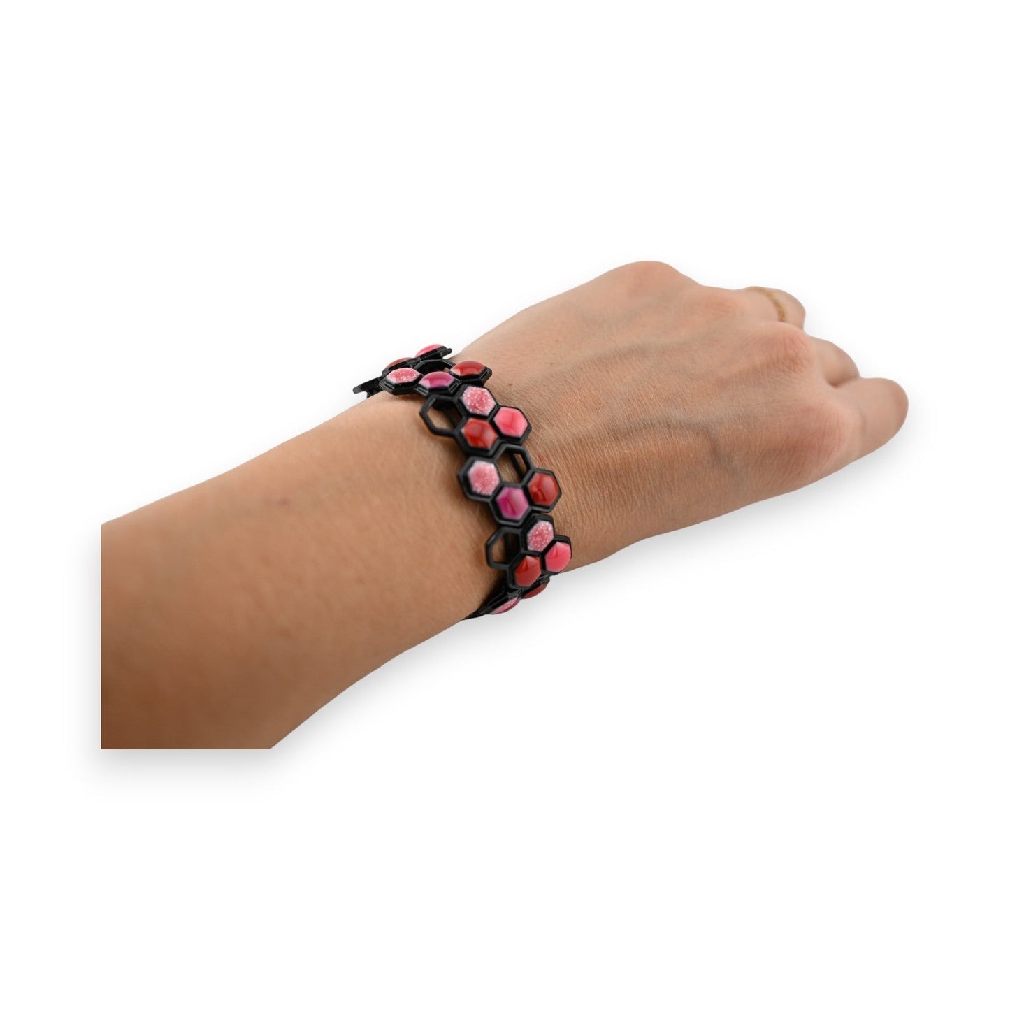 Elastisches Wabenarmband in Schwarz mit rosa und roten Sechsecken, am Handgelenk getragen, auf weißem Hintergrund