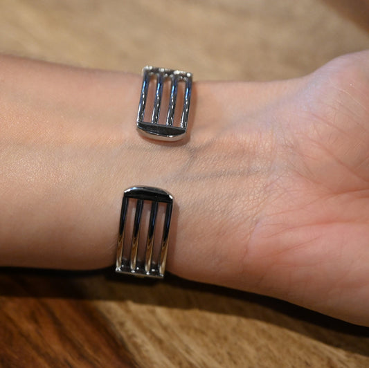 Nahaufnahme eines silbernen Armbands mit zwei rechteckigen Elementen auf einer Hand, die auf Holzuntergrund liegt