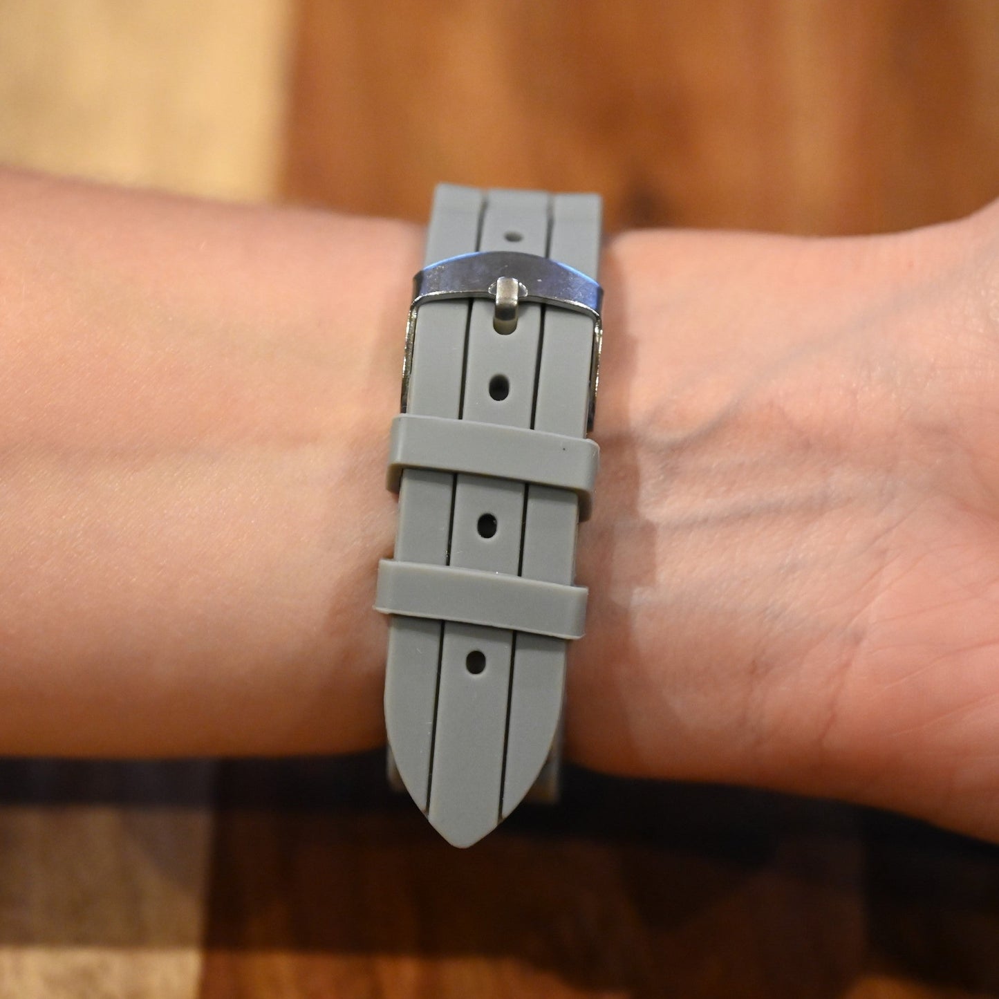 Graues Silikonarmband einer Armbanduhr am Handgelenk, mit silberner Schnalle und strukturiertem Design