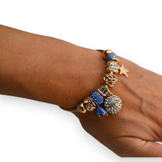 Goldenes Armband mit blauen Strass-Charms und Anhängern auf dunkler Haut, eleganter Schmuck mit Sterndetail