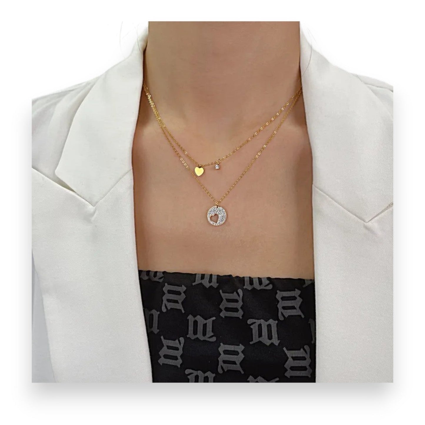 Doppelte vergoldete Halskette mit Herzanhängern, goldenem Strass-Kreis und kleinem Stein auf weißem Blazer und Muster-Top