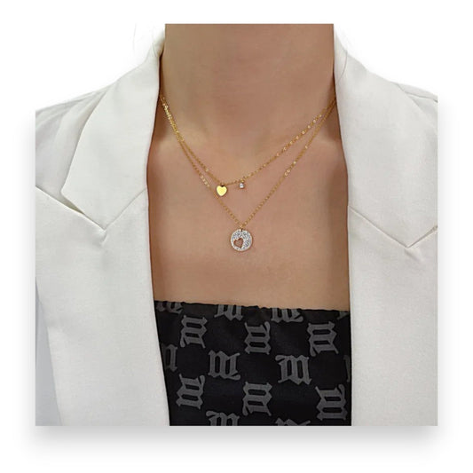 Doppelte vergoldete Halskette mit Herzanhängern, goldenem Strass-Kreis und kleinem Stein auf weißem Blazer und Muster-Top