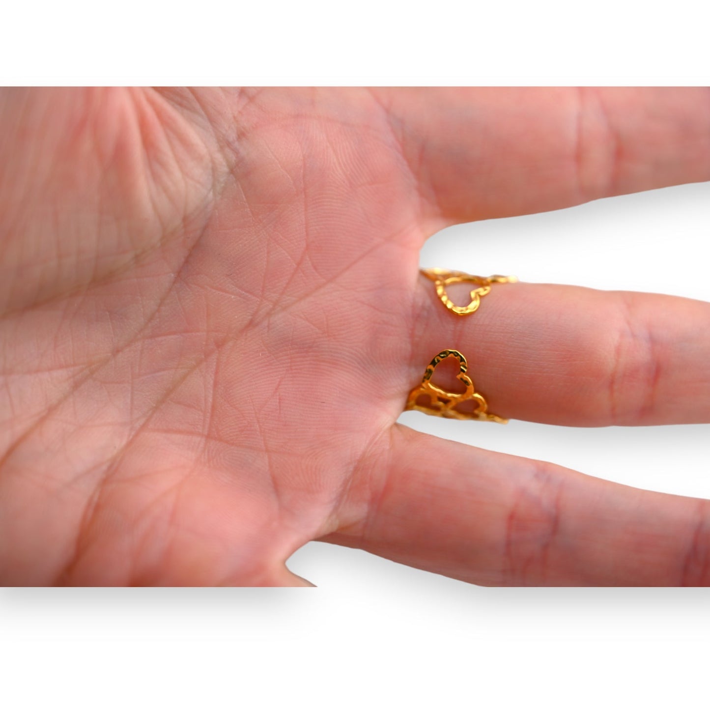 Nahaufnahme einer Hand mit goldenem Ring, der zwei kleine Herzen zeigt. Detaillierte Ansicht der Handfläche und Finger.