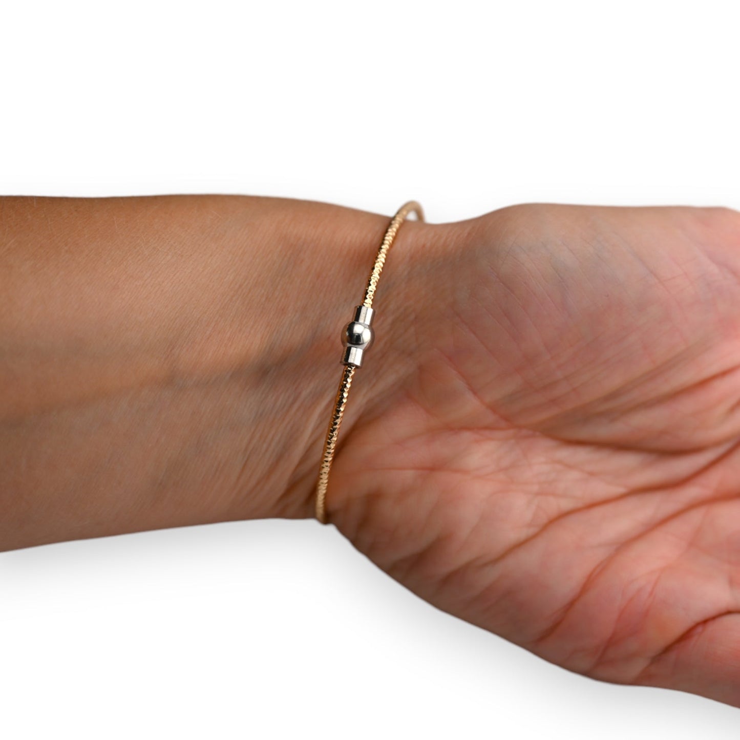 Zierlicher goldener Armreif mit silbernem Kugeldetail auf Handgelenk, filigrane Schmuckgestaltung für elegantes Aussehen