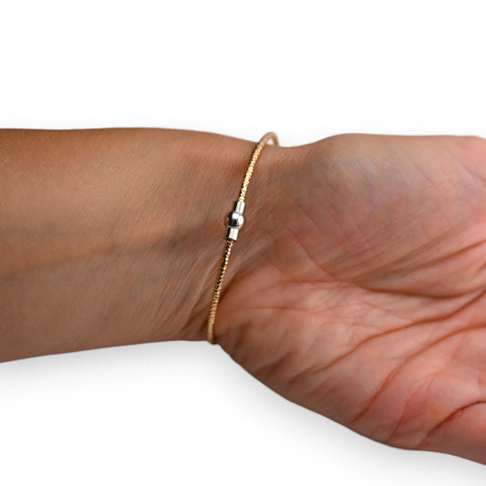 Zierlicher goldener Armreif mit silbernem Kugeldetail auf Handgelenk, filigrane Schmuckgestaltung für elegantes Aussehen