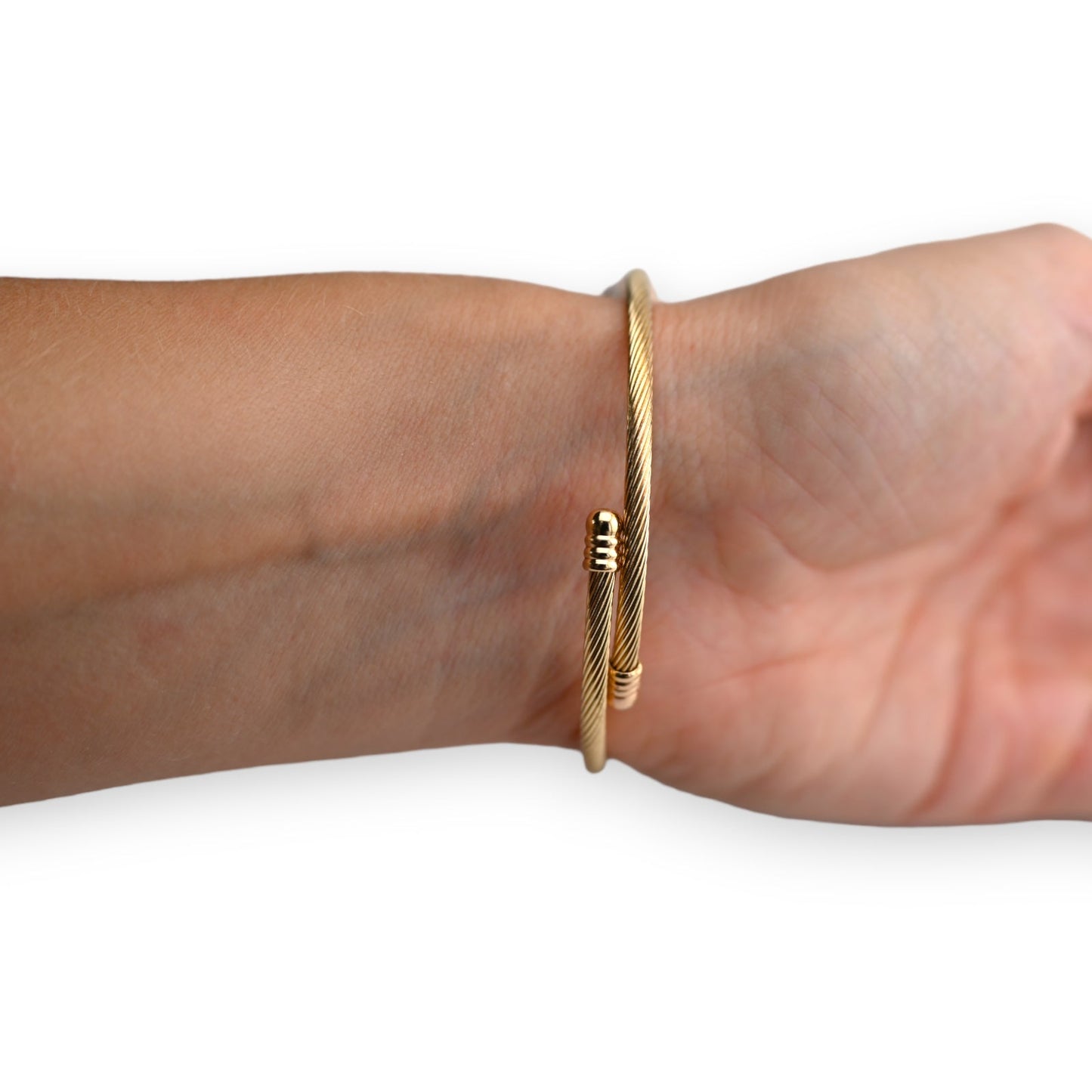 Goldenes Armreif aus gedrehtem Metall am Handgelenk, minimalistisches Design mit kleinen Goldperlen als Akzent