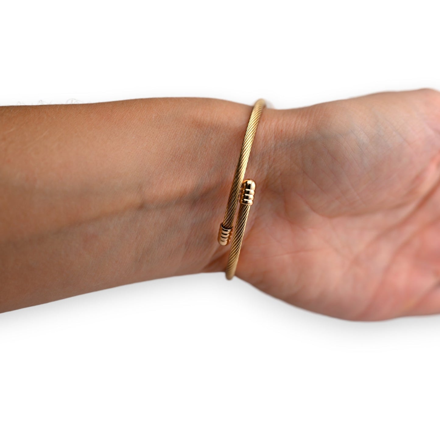 Goldenes Armreif aus gedrehtem Metall mit kleinen Kugel-Charms, getragen am Handgelenk einer Person mit hellbrauner Haut
