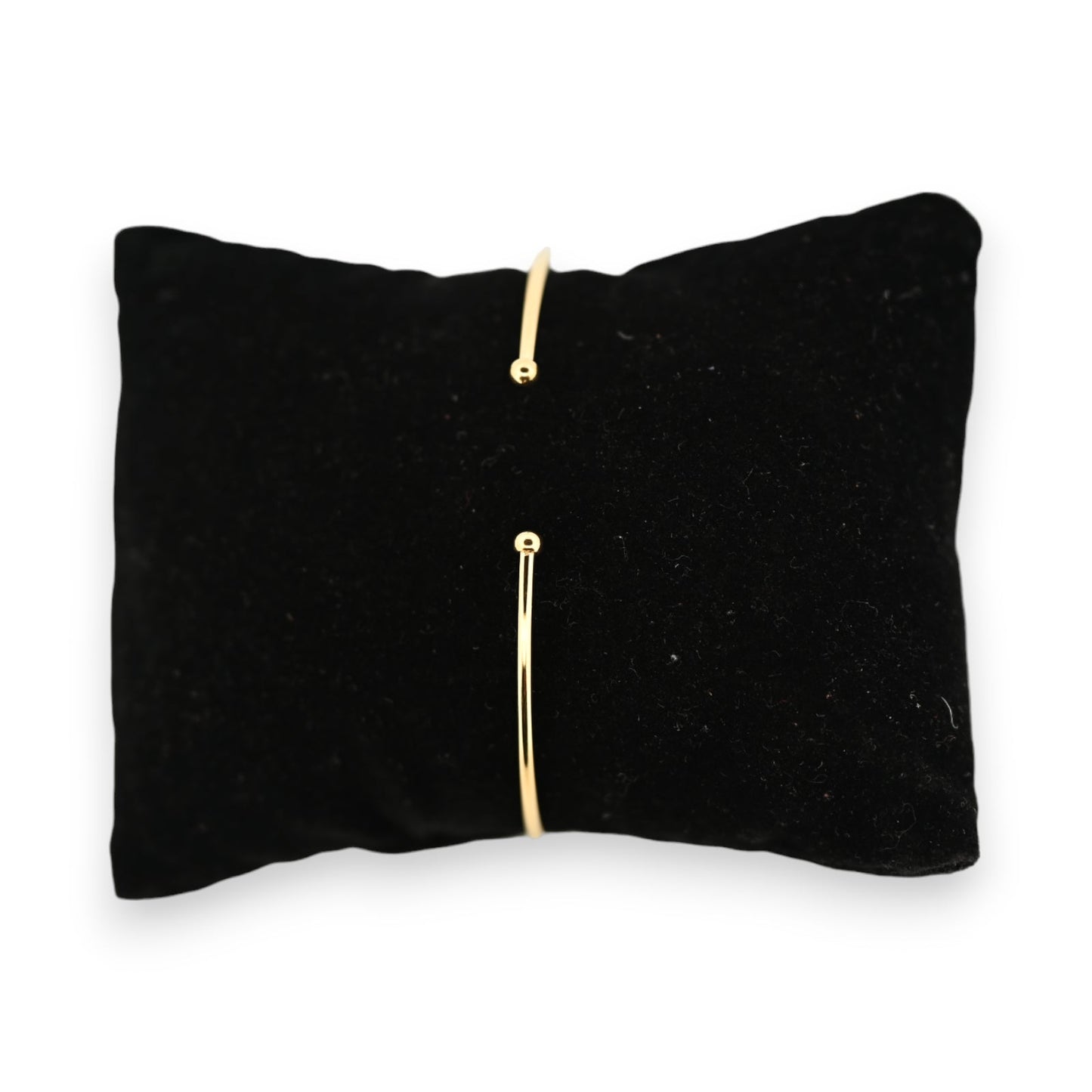 Minimalistisches goldenes Armreif auf schwarzem Samtkissen, offene Form mit zwei kleinen Kugeln an den Enden