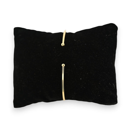 Minimalistisches goldenes Armreif auf schwarzem Samtkissen, offene Form mit zwei kleinen Kugeln an den Enden