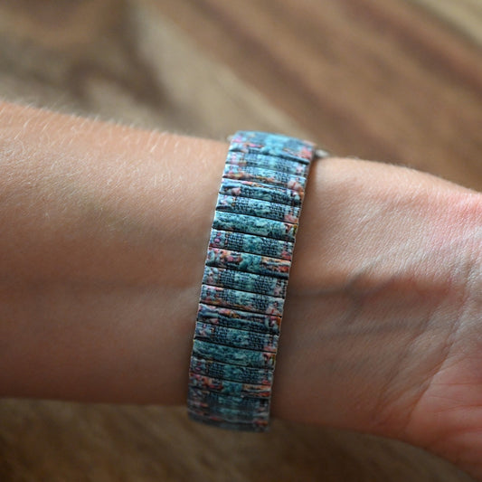 Armband mit grün-blauem Wasserstrick-Effekt auf einem Handgelenk. Detailliertes Muster aus kleinen Rechtecken.