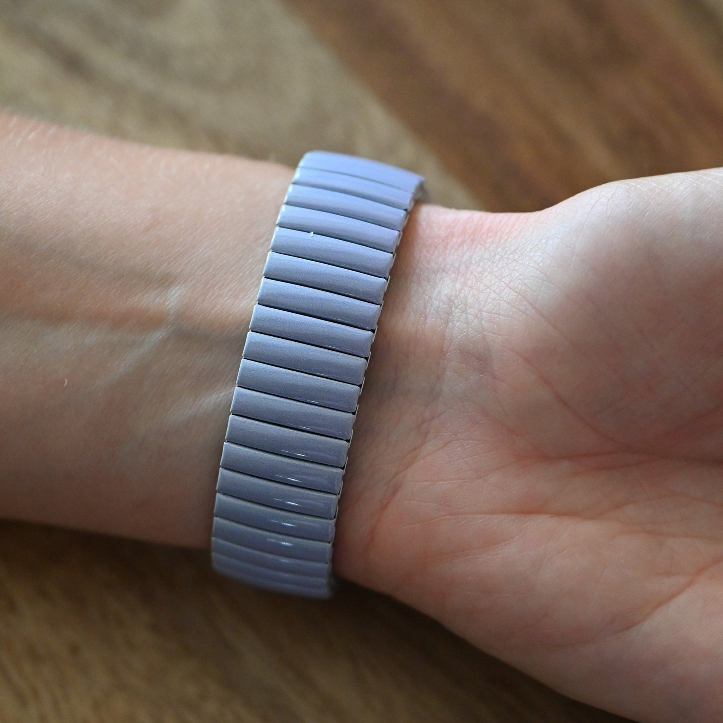 Hellgraues, elastisches Armband mit horizontalen Rillen am Handgelenk einer Person auf Holzuntergrund