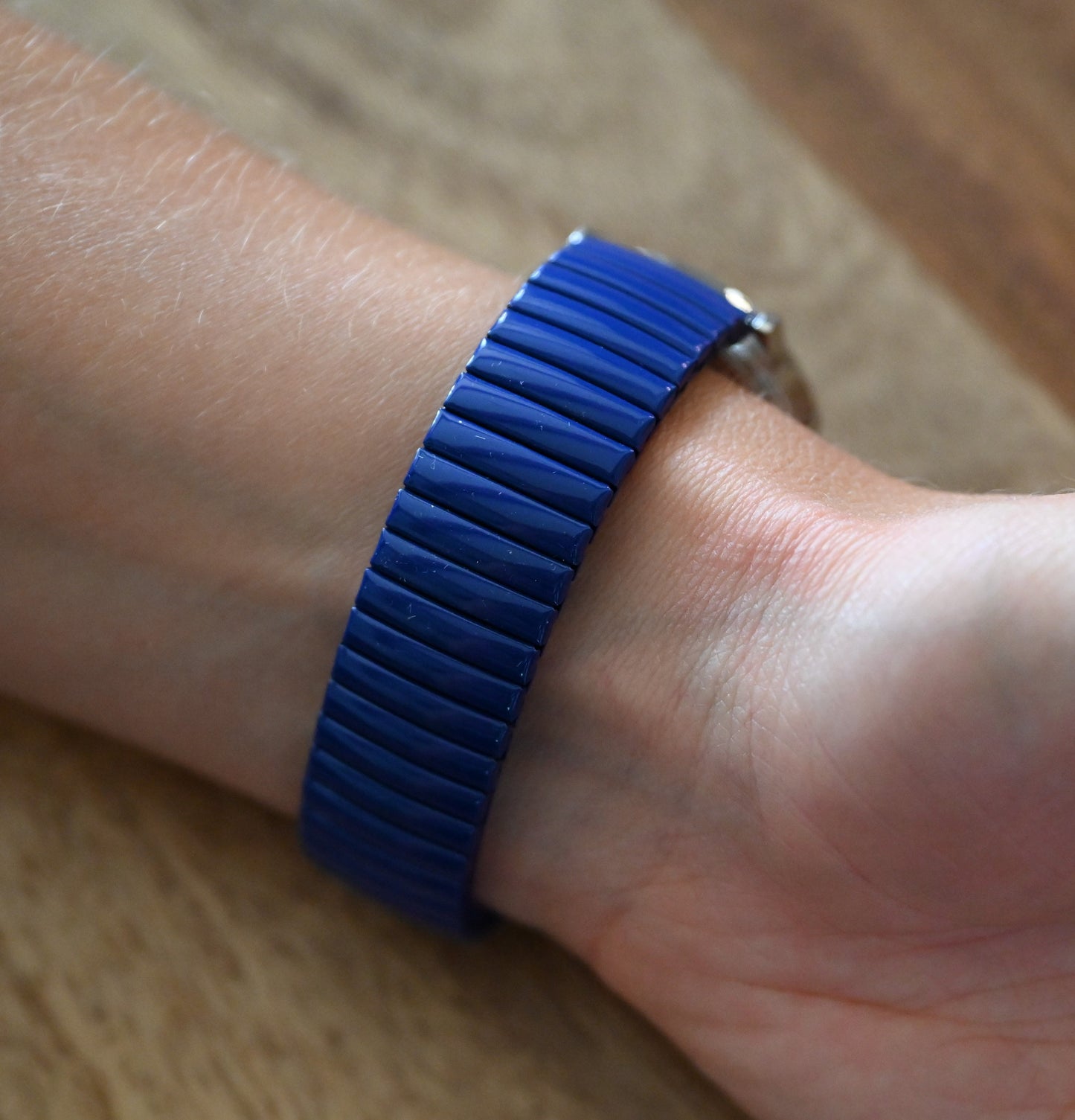 Blaues elastisches Armband aus länglichen Elementen an einem Handgelenk auf hölzernem Untergrund
