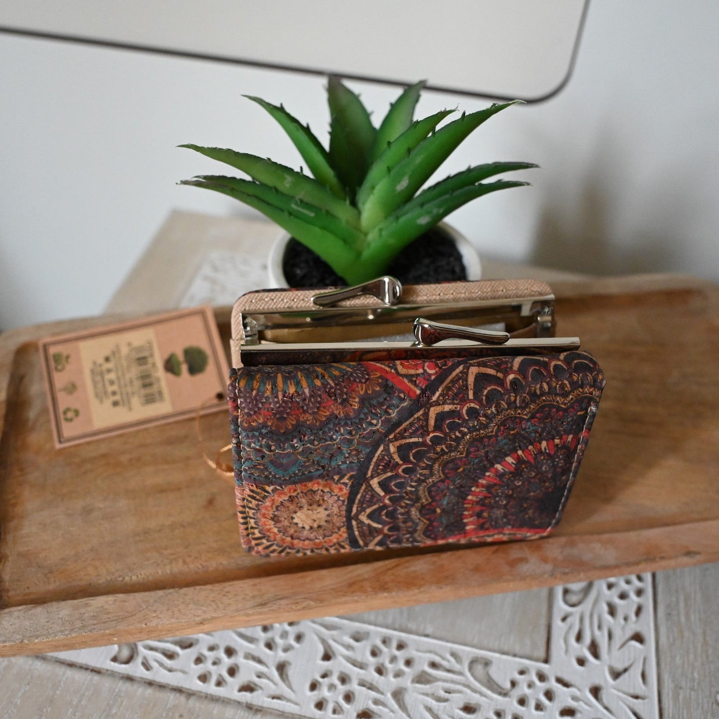 Kompakte Ledergeldbörse mit buntem Mandala-Muster auf Holztisch neben Sukkulente und Kartonverpackung