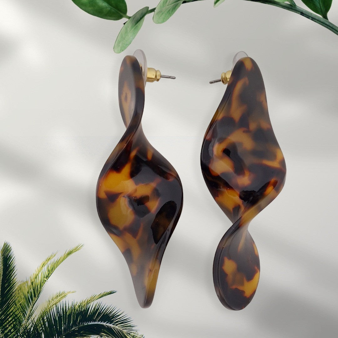 Gedrehte Ohrhänger in Leopardenmuster-Optik, braun-orange marmoriert, vor hellem Hintergrund mit Blattdekoration