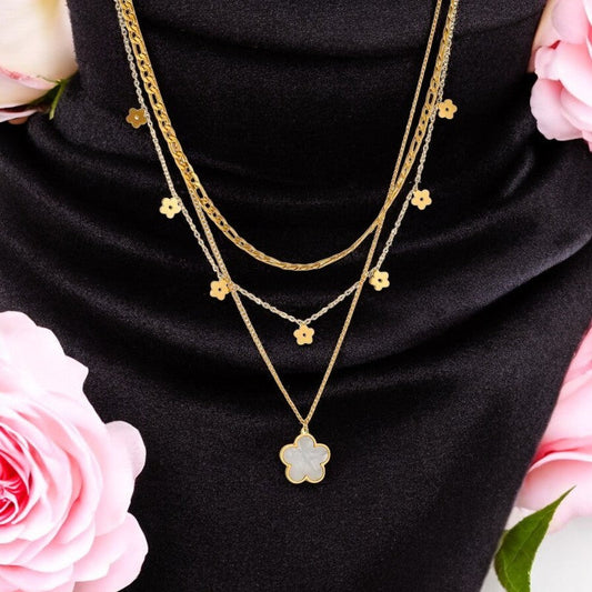 Mehrreihige goldene Halskette mit Blumenanhängern auf schwarzem Stoff, umgeben von rosa Rosen, elegantes Schmuckstück