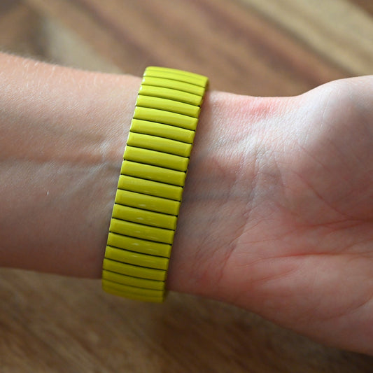 Gelbes elastisches Armband aus schmalen Streifen am Handgelenk einer Person auf Holzuntergrund