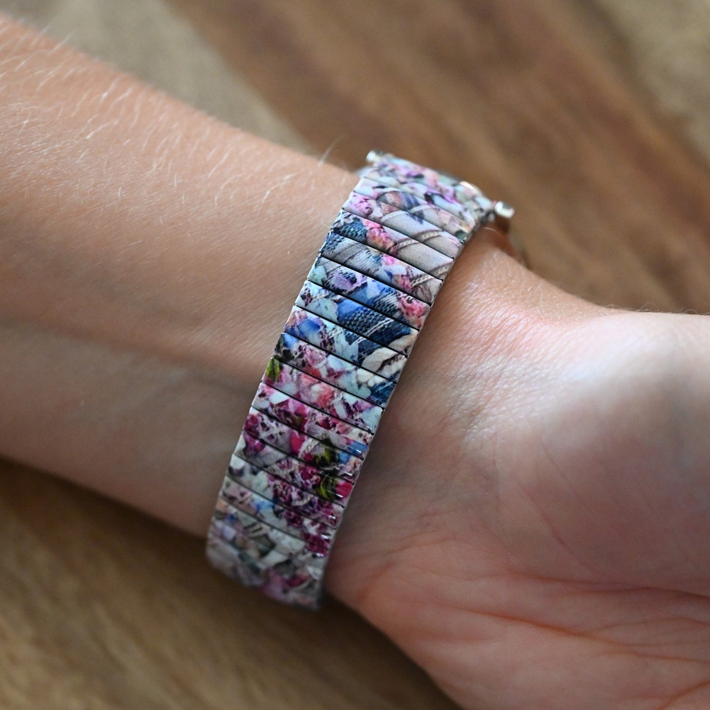 Dehnbares Armband mit buntem Pastell-Patchwork-Muster auf einem Handgelenk, Nahaufnahme auf Holzuntergrund