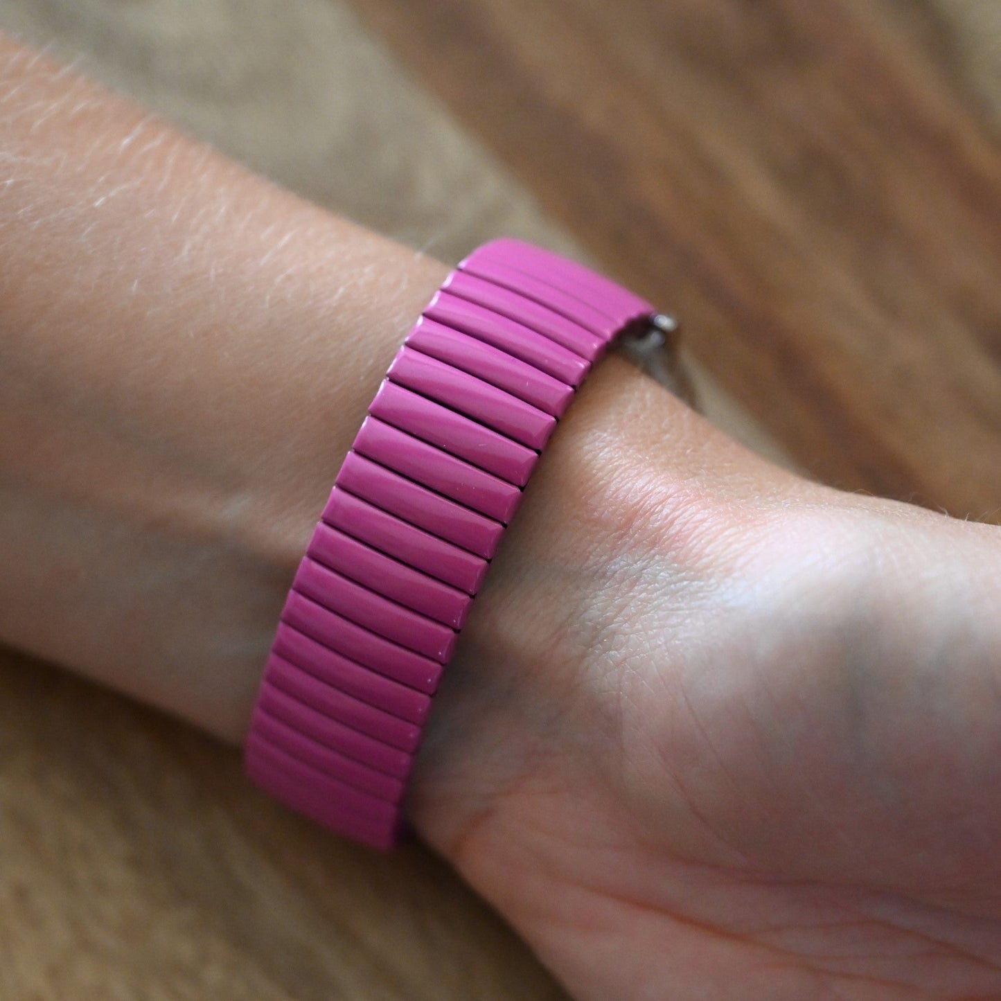 Rosa elastisches Armband mit parallelen Rillen auf einem Handgelenk, gegen Holzoberfläche fotografiert