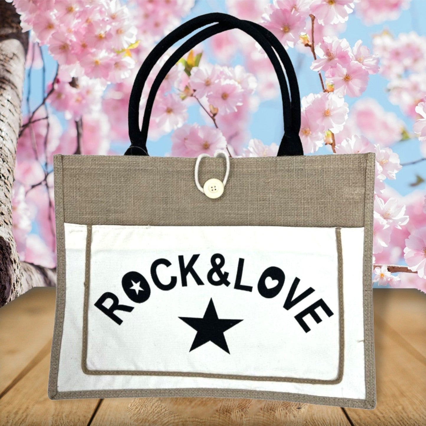 Tote Bag mit 'Rock & Love' Aufdruck vor blühenden Kirschblüten. Beige Tasche mit schwarzen Griffen und Sternmotiv.