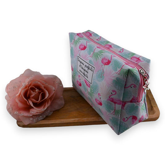 Rosa Flamingo Toilettentasche mit tropischem Muster neben rosa Blume auf Holzuntergrund, Reise-Kosmetiktasche