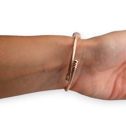 Elegantes kupferfarbenes Armband mit feinem Drahtdesign, dezent um ein Handgelenk geschlungen auf weißem Hintergrund