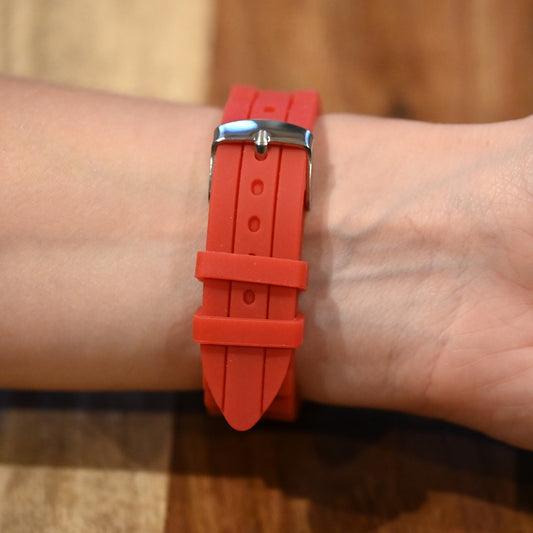 Rotes Silikonarmband mit Metallschnalle an einem Handgelenk, Nahaufnahme auf Holzuntergrund