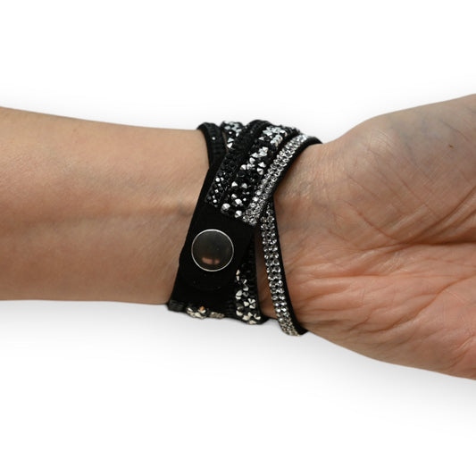 Schwarzes Doppelarmband mit weißen Strasssteinen und silbernem Knopf am Handgelenk getragen, elegant und glitzernd