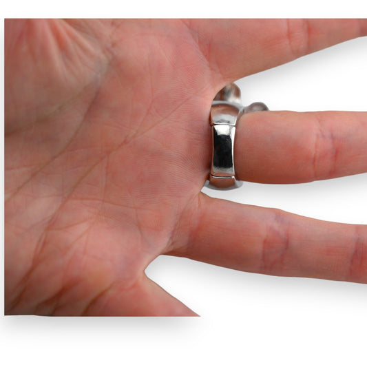 Silberner Ring mit breiter, glänzender Oberfläche am Finger einer Hand vor weißem Hintergrund