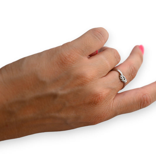 Silberner Knotenring aus Stahl an Hand mit rot lackierten Fingernägeln, eleganter Schmuck auf weißem Hintergrund