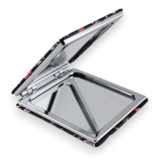 Aufgeklappter Taschenspiegel mit silbernem Rahmen und floralem Muster, geöffnet zeigt er einen rechteckigen Spiegel