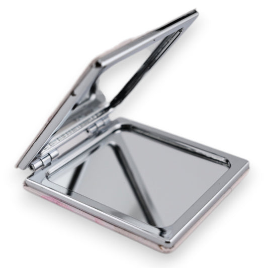 Aufgeklappter quadratischer Taschenspiegel mit silbernem Rahmen und rosa Unterseite, reflektiert Licht auf weißem Hintergrund